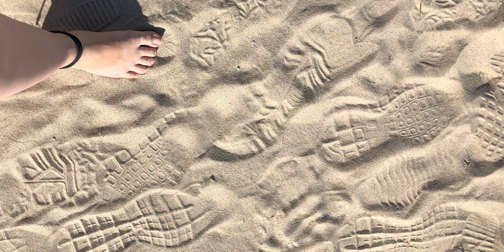 Foto vom Strand mit Fuß- und Schuhabdrücken und mein Fuß - symbolhaft für ökologischer Fußabdruck