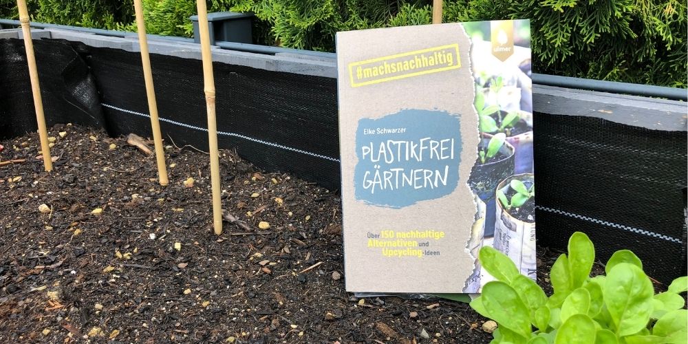 Das Buch "Plastikfrei Gärtnern" steht im Blumenbeet