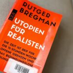 Das Buch "Utopien für Realisten" von Rutger Bregman liegt auf einer grauen Unterlage