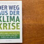 Das Buch "Der Weg aus der Klimakrise" liegt auf einem dunklen Holzboden.