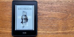 Auf einem Holzboden liegt ein eBook Reader darauf ist das Cover von die Abschaffung des Todes zu sehen.