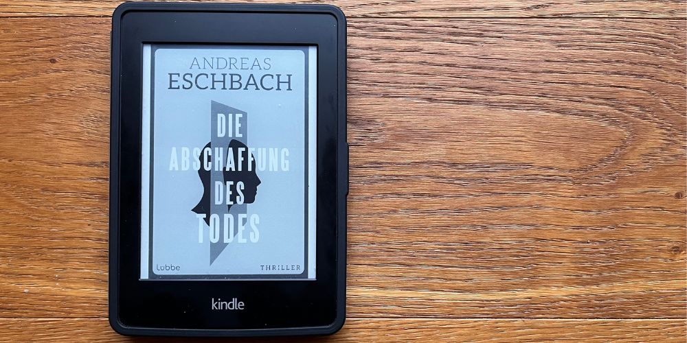 Auf einem Holzboden liegt ein eBook Reader darauf ist das Cover von die Abschaffung des Todes zu sehen.